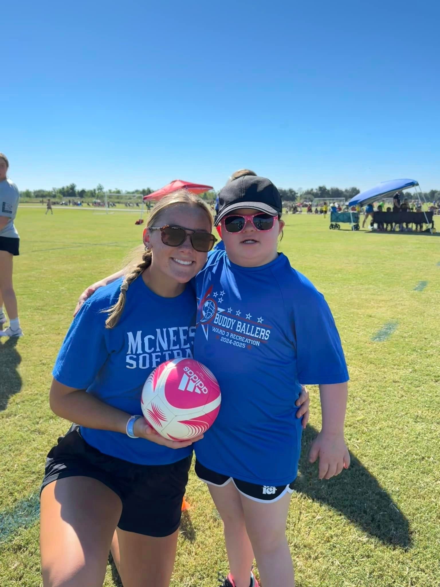 Two girls are standing next to each other on a field holding a ball.