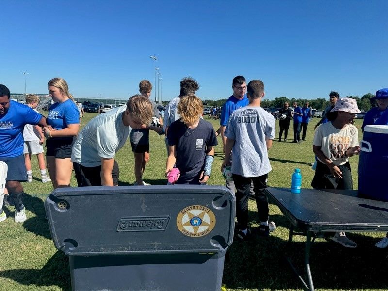 A group of people are standing around a trash can on a field.