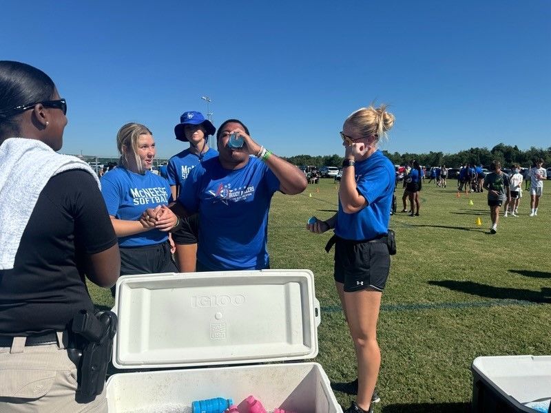 A group of people are standing around a cooler in a field.