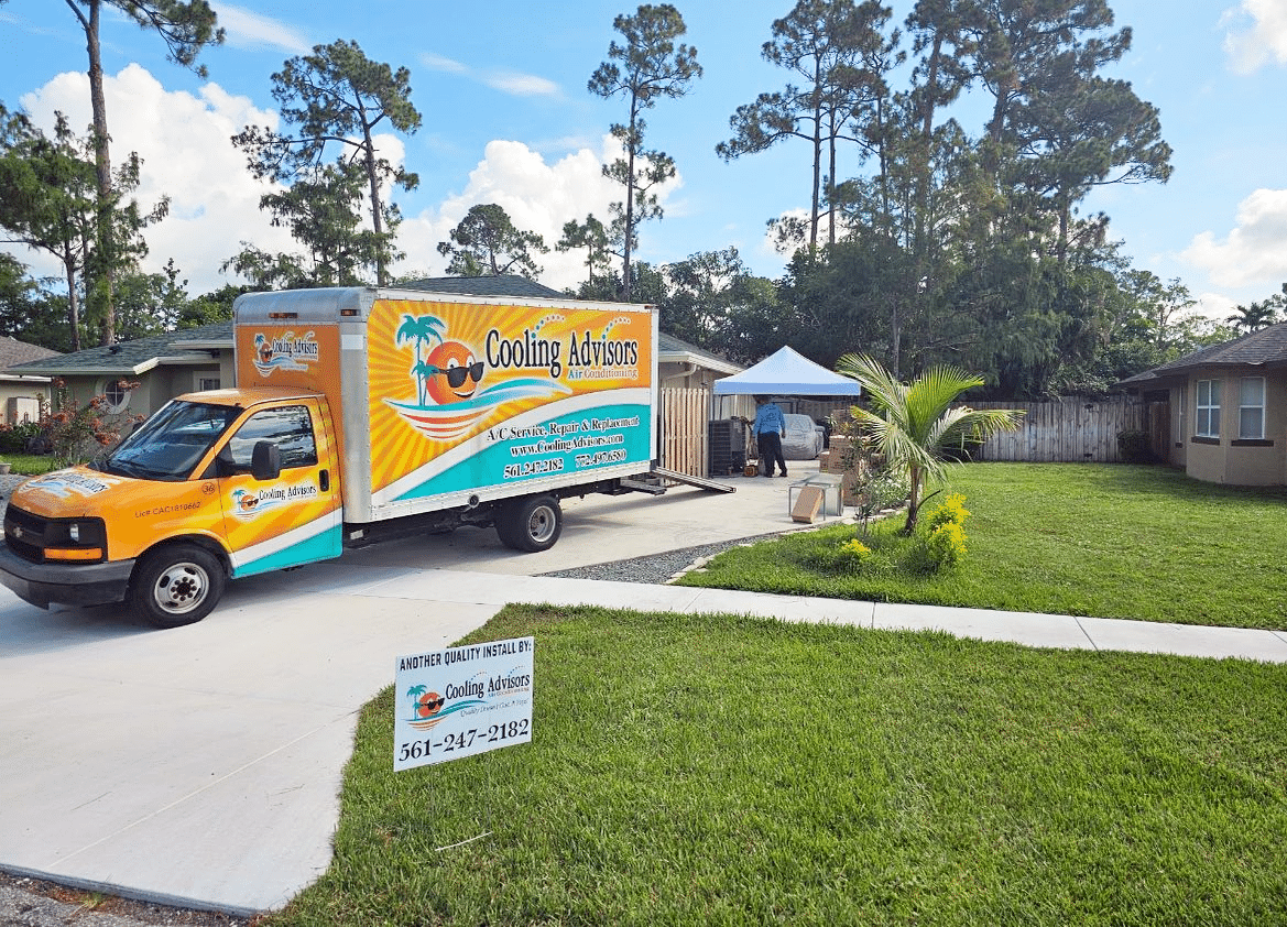 Moving truck parked in front of a house, sign in front, person unloading items, and a canopy.