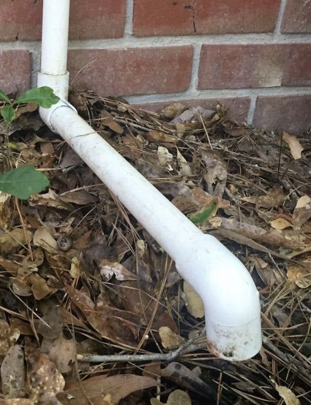 White PVC pipes extending from a brick wall into ground covered in leaves and twigs.