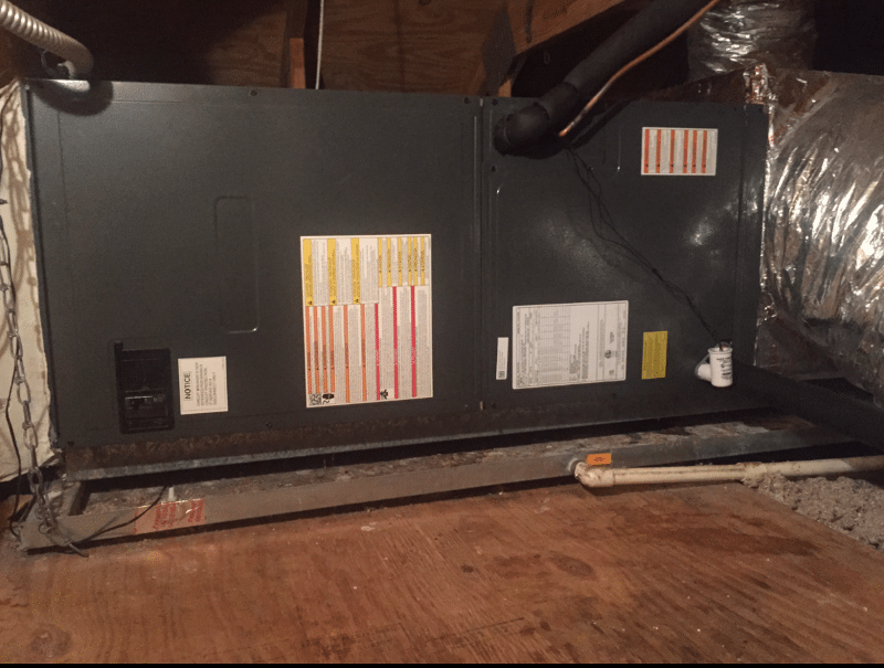 Furnace in a wooden-floored attic, dark metal exterior, with ductwork and various labels.