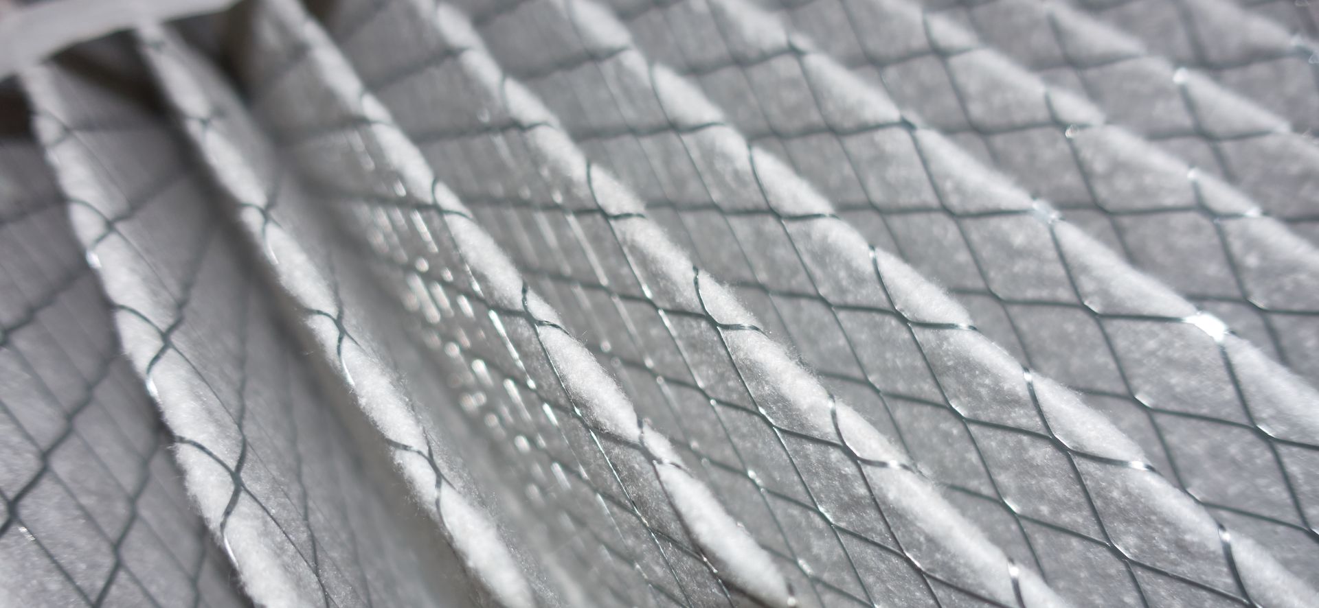 Close-up of a pleated air filter with a diamond-patterned metal mesh.