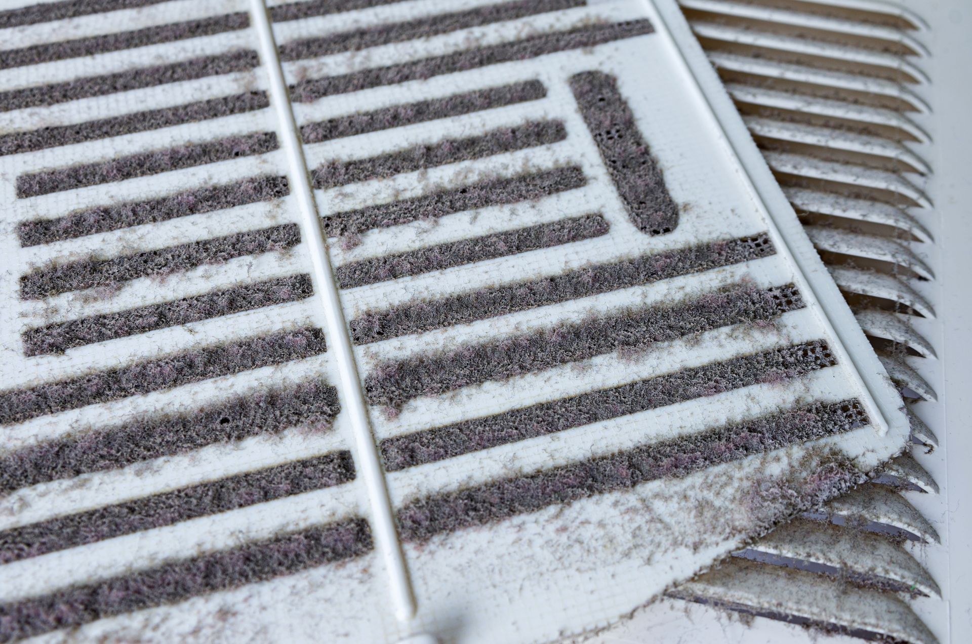 Close-up of a dusty air conditioning filter with raised horizontal bars and a white frame.