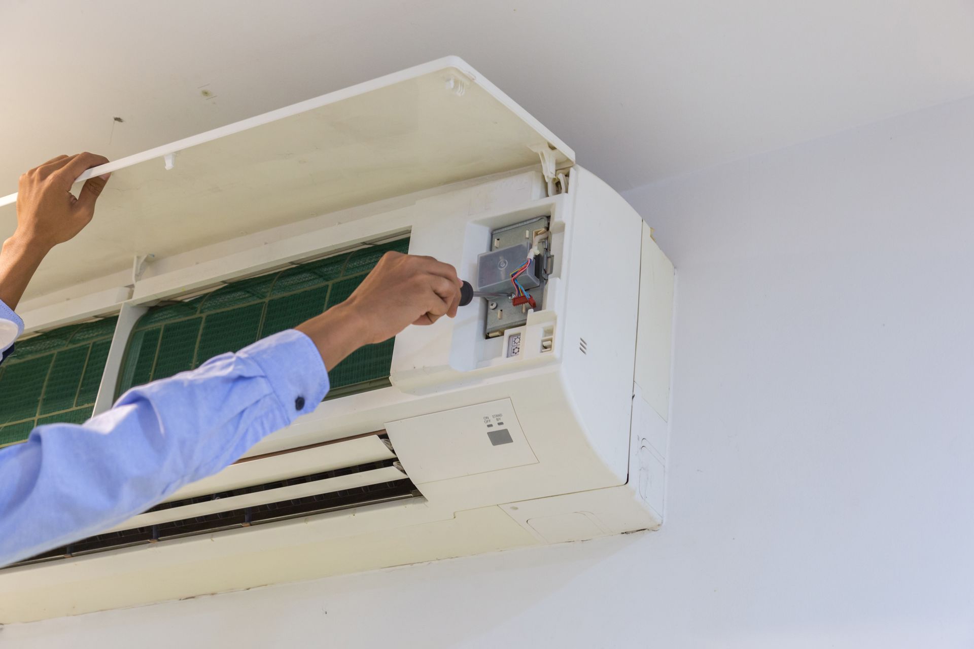Person repairs a wall-mounted air conditioner, removing the cover with a screwdriver.