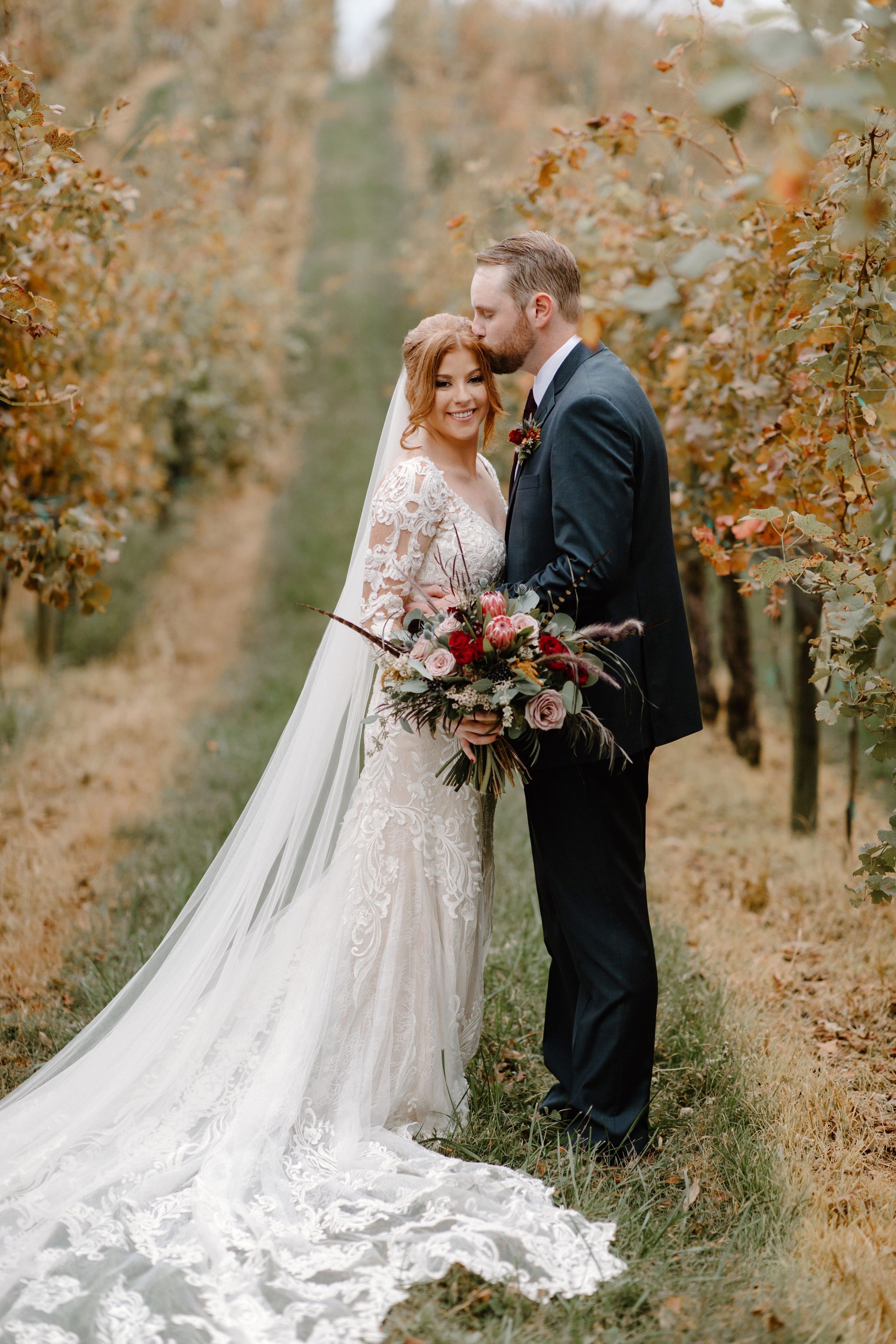 A bride and groom are posing for a picture in a vineyard.