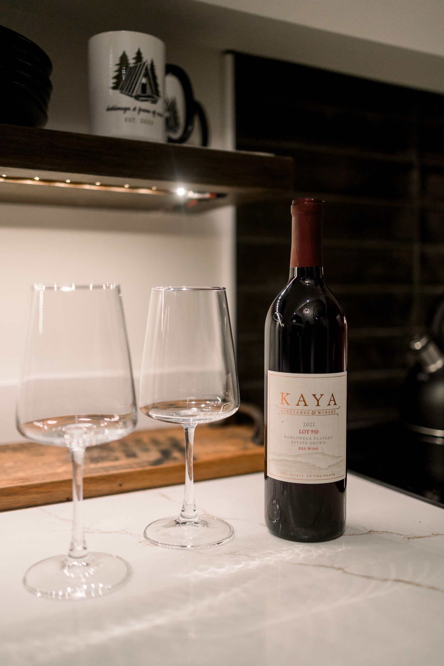 A bottle of lava wine is sitting on a counter next to two wine glasses.