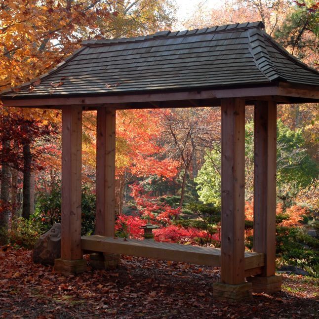 A wooden shelter with a roof in the middle of a forest