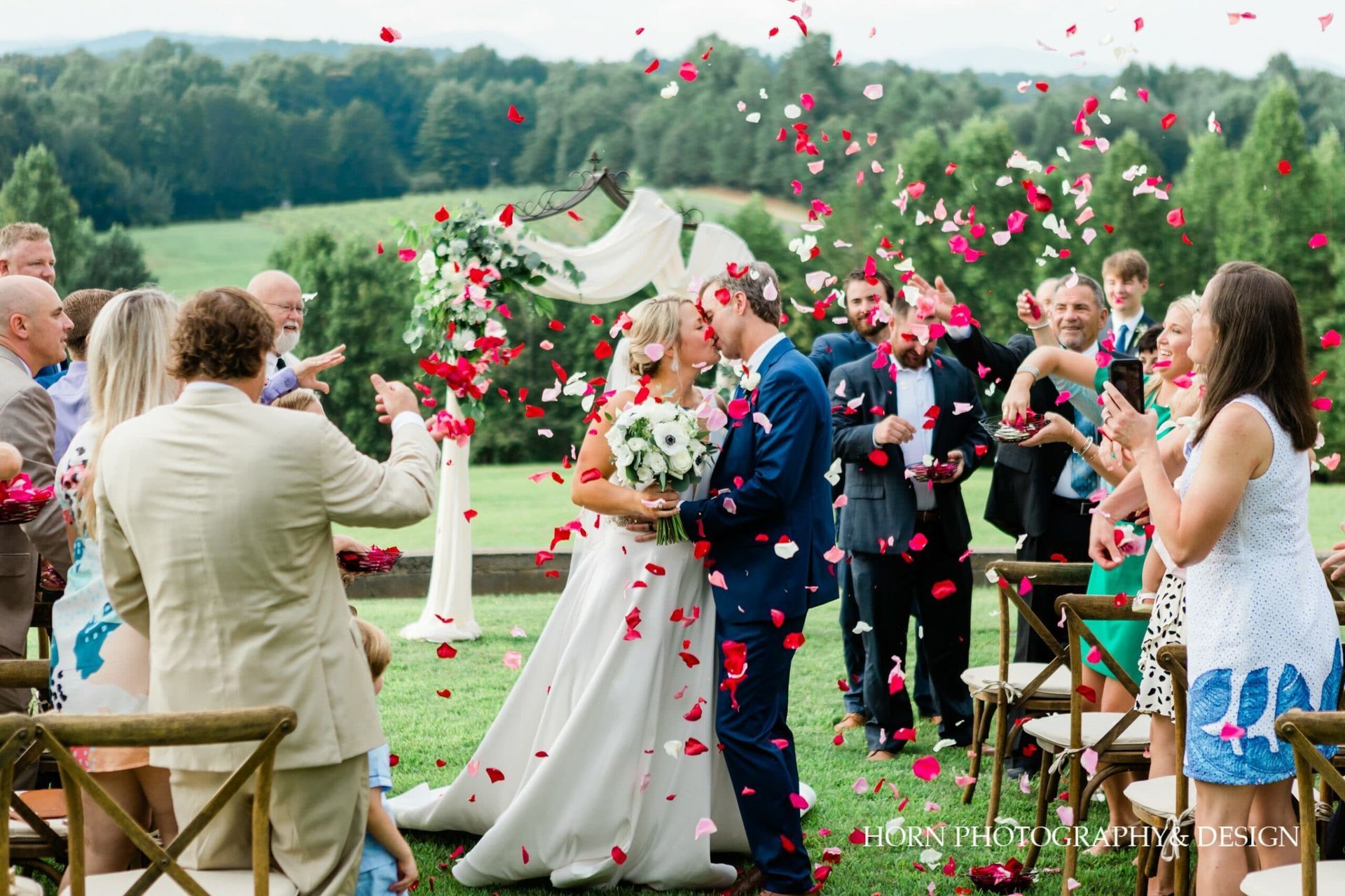 A bride and groom are kissing while their wedding guests throw confetti at them.