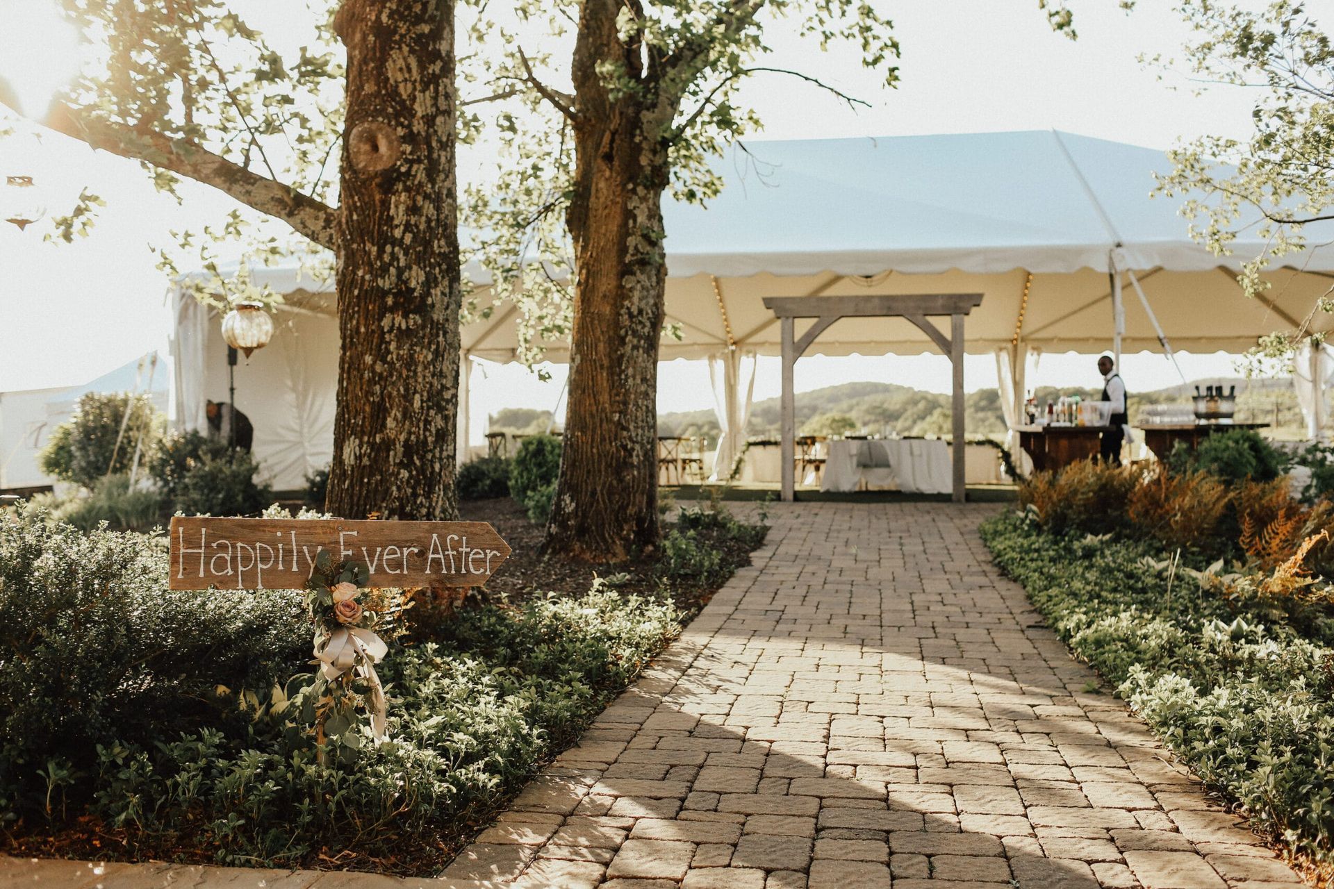 A brick walkway leading to a large tent surrounded by trees.