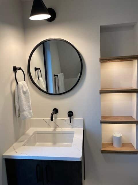 A bathroom with a sink , mirror and shelves.