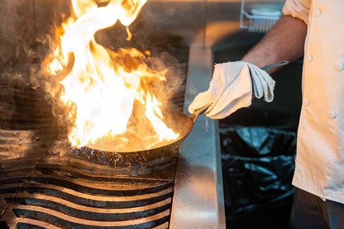 A chef is cooking food on a stove with flames coming out of it.