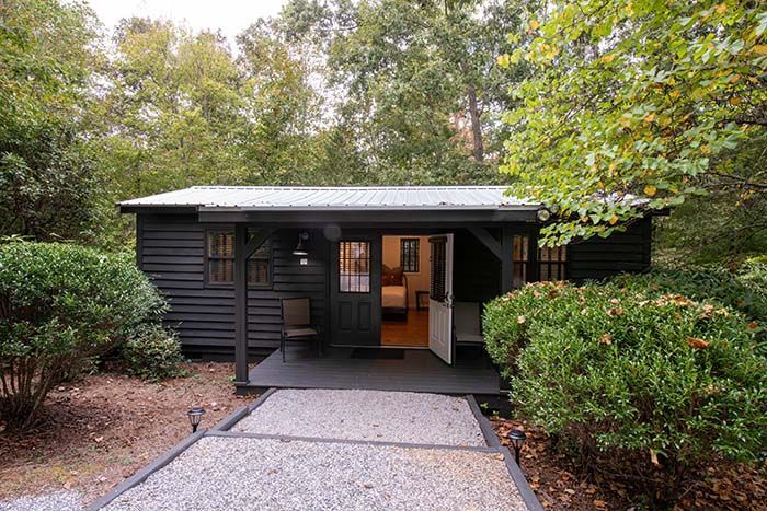 A small black house is surrounded by trees and bushes.