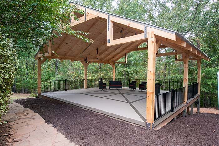 A large wooden pavilion with a concrete floor and chairs underneath it.