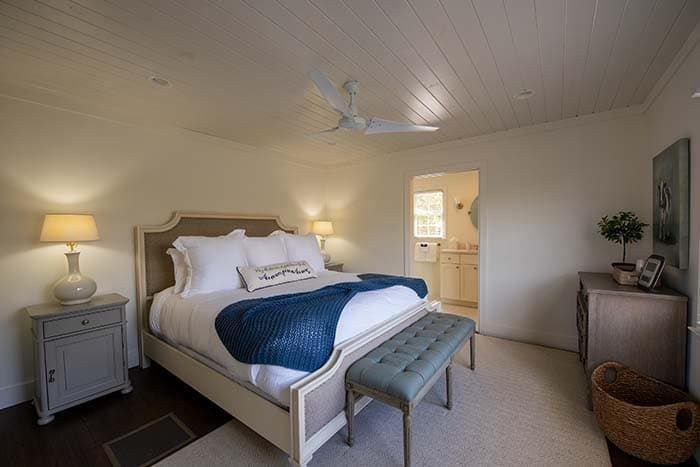 A bedroom with a bed , nightstand , bench and ceiling fan.
