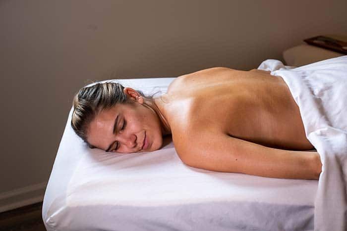 A woman is laying on a massage table with her eyes closed.