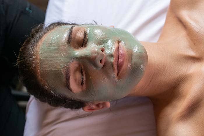 A woman is laying on a bed with a green mask on her face.