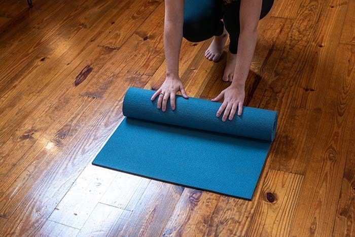 A person is rolling a yoga mat on a wooden floor.