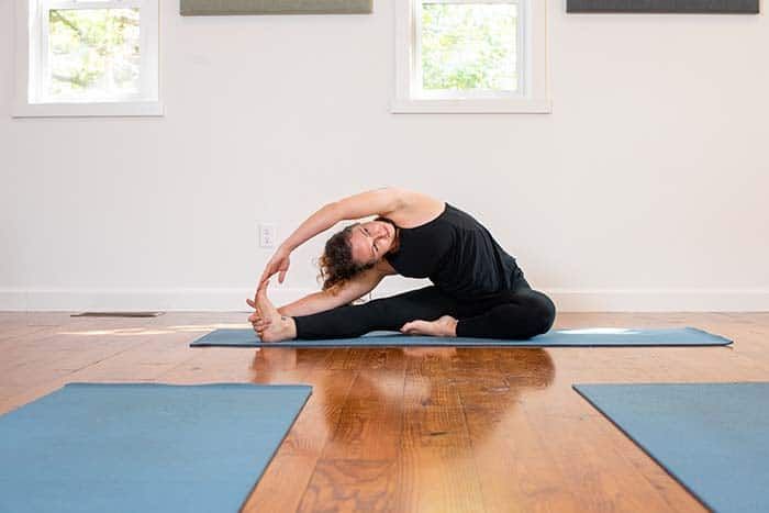 A woman is stretching on a yoga mat in a room.