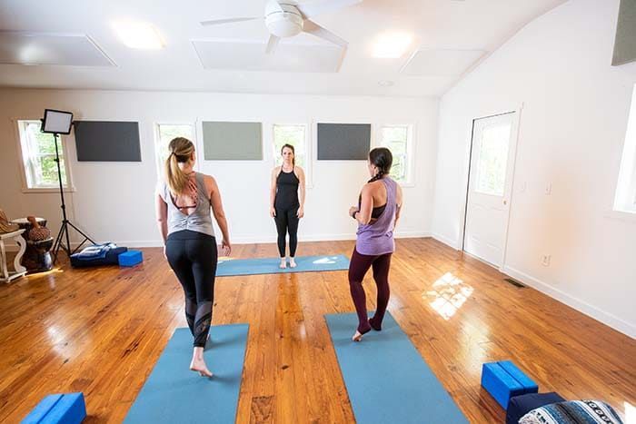 Three women are standing on yoga mats in a room.