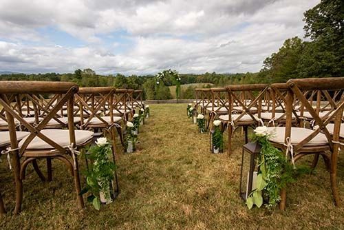 A row of wooden chairs are lined up in a field for a wedding ceremony.