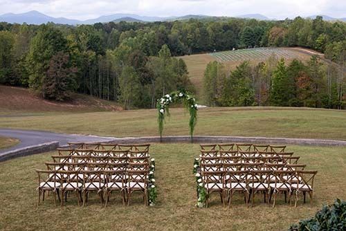 A row of chairs are lined up in a field with mountains in the background.