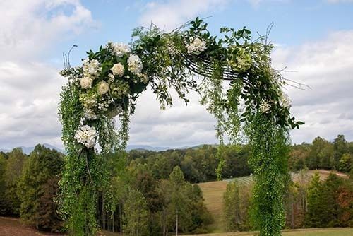 A wedding arch decorated with white flowers and greenery in a field.