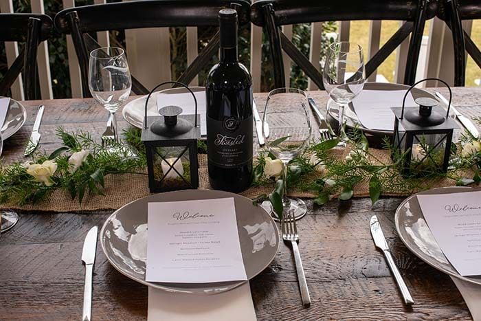 A wooden table with plates , utensils , and a bottle of wine on it.