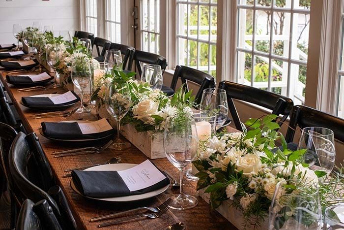 A long wooden table with plates , glasses , and flowers on it.
