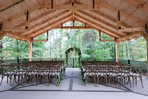 A wooden pavilion with rows of chairs under a wooden roof.