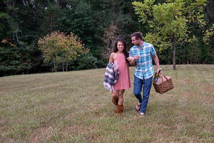 A man and a woman are walking in a field with a picnic basket.