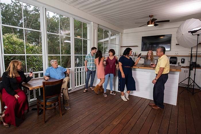 A group of people are standing on a porch drinking wine.