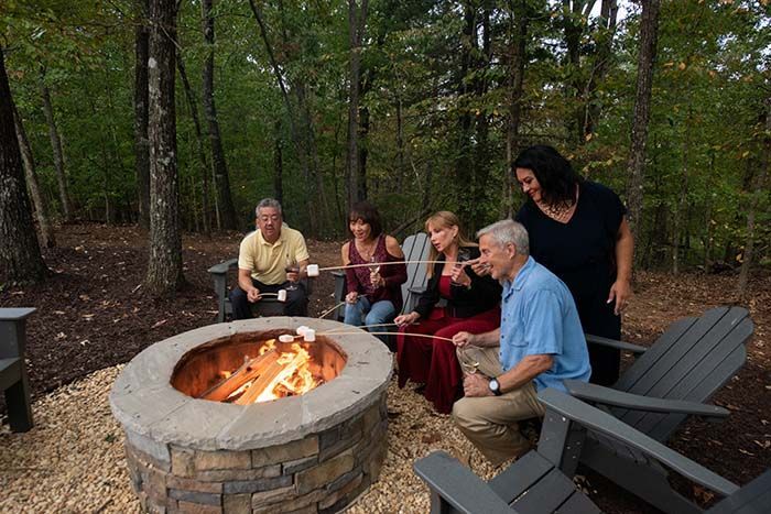 A group of people are sitting around a fire pit roasting marshmallows.