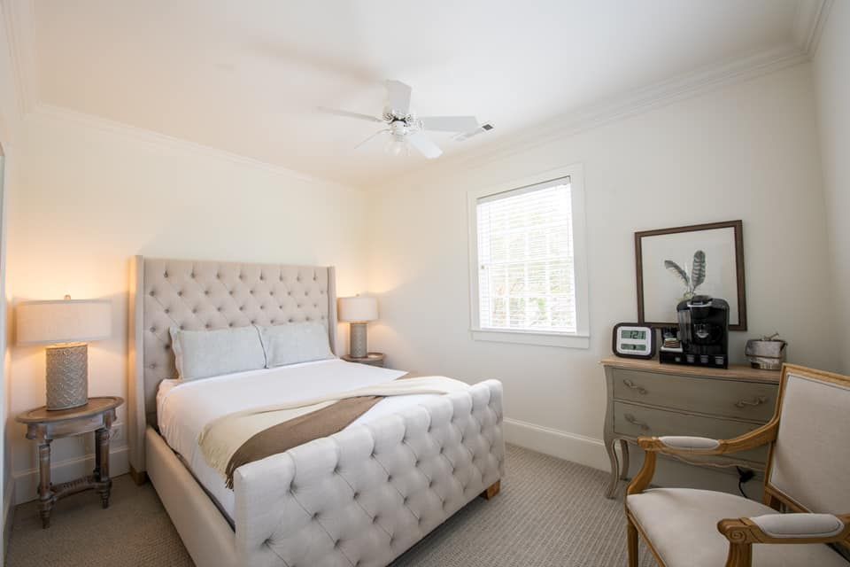 A bedroom with a bed , chair , nightstand , desk and ceiling fan.