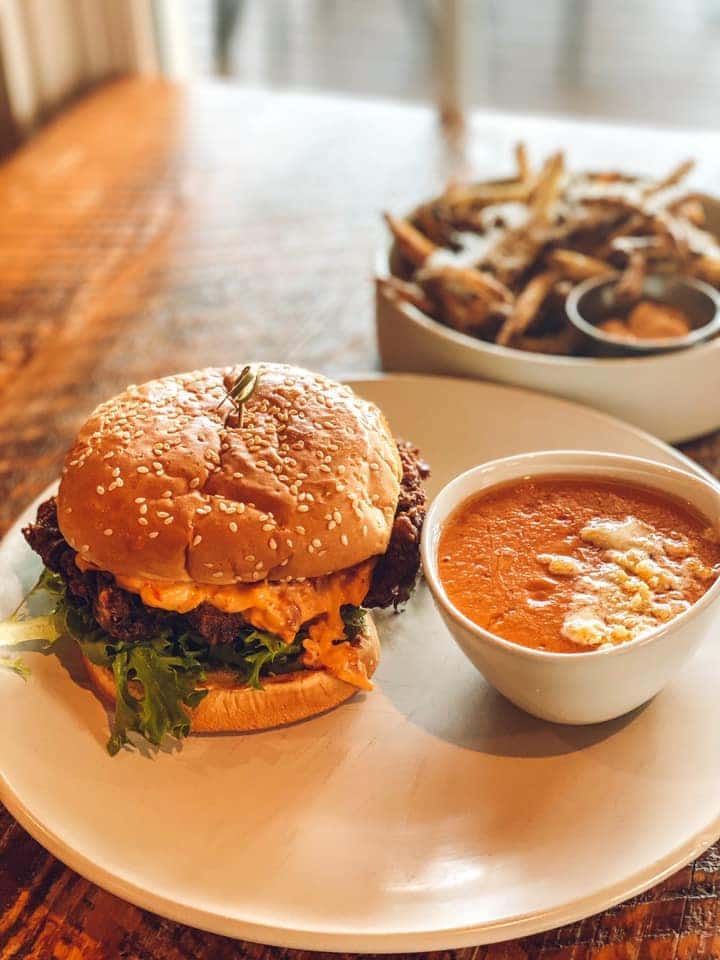 A hamburger and a bowl of soup are on a plate on a table.