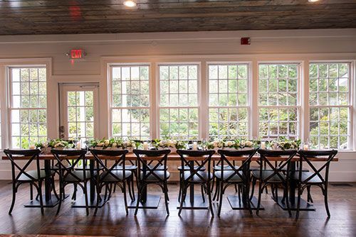 A long table and chairs in a room with lots of windows.