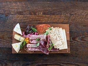 A wooden cutting board topped with meat and cheese on a wooden table.