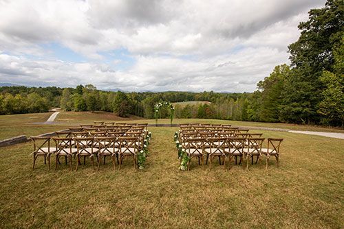 A row of wooden chairs are lined up in a field for a wedding ceremony.