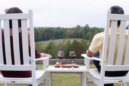 A man and a woman are sitting in white chairs with wine glasses on a table.