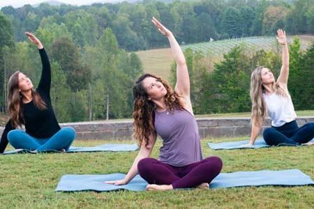 Three women are sitting on yoga mats in a field.