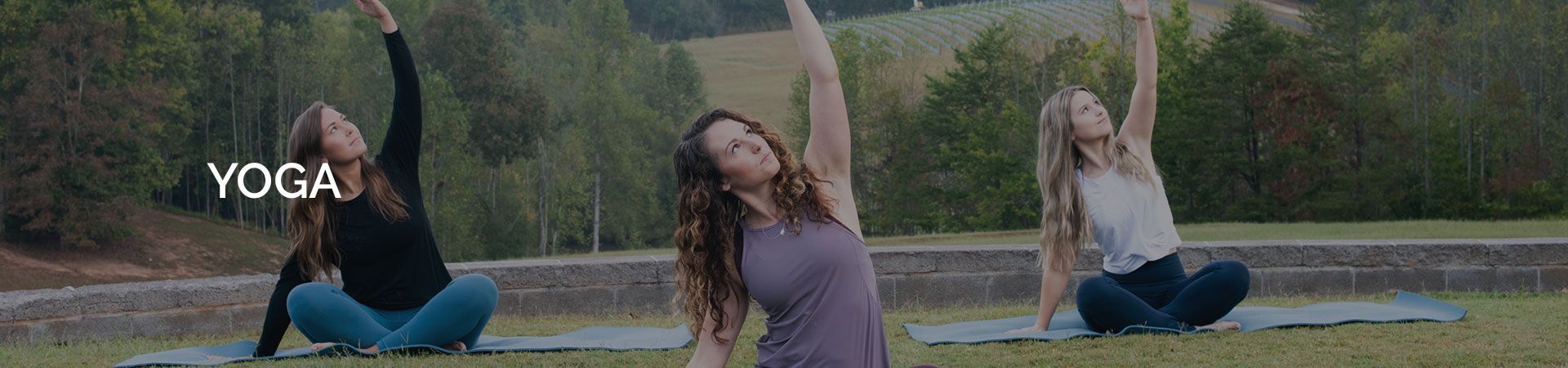Three women are doing yoga in a park with their arms in the air.