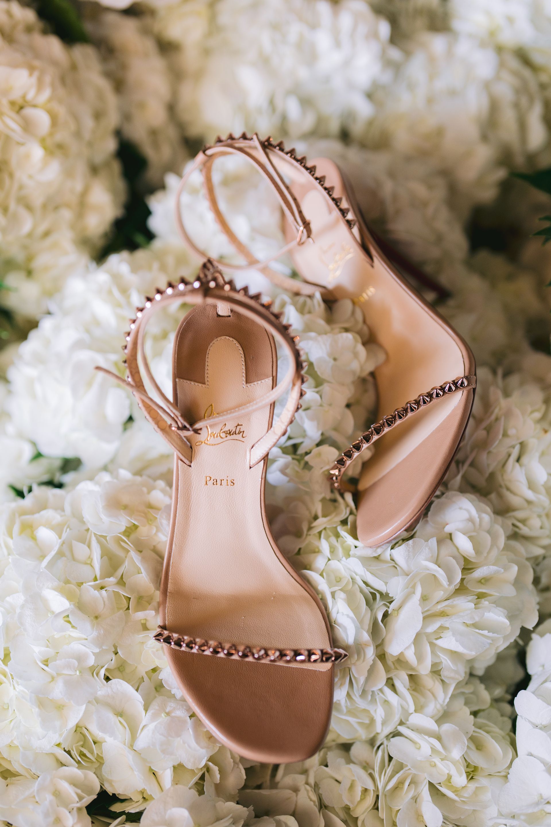 A pair of wedding shoes sitting on top of a pile of white flowers.