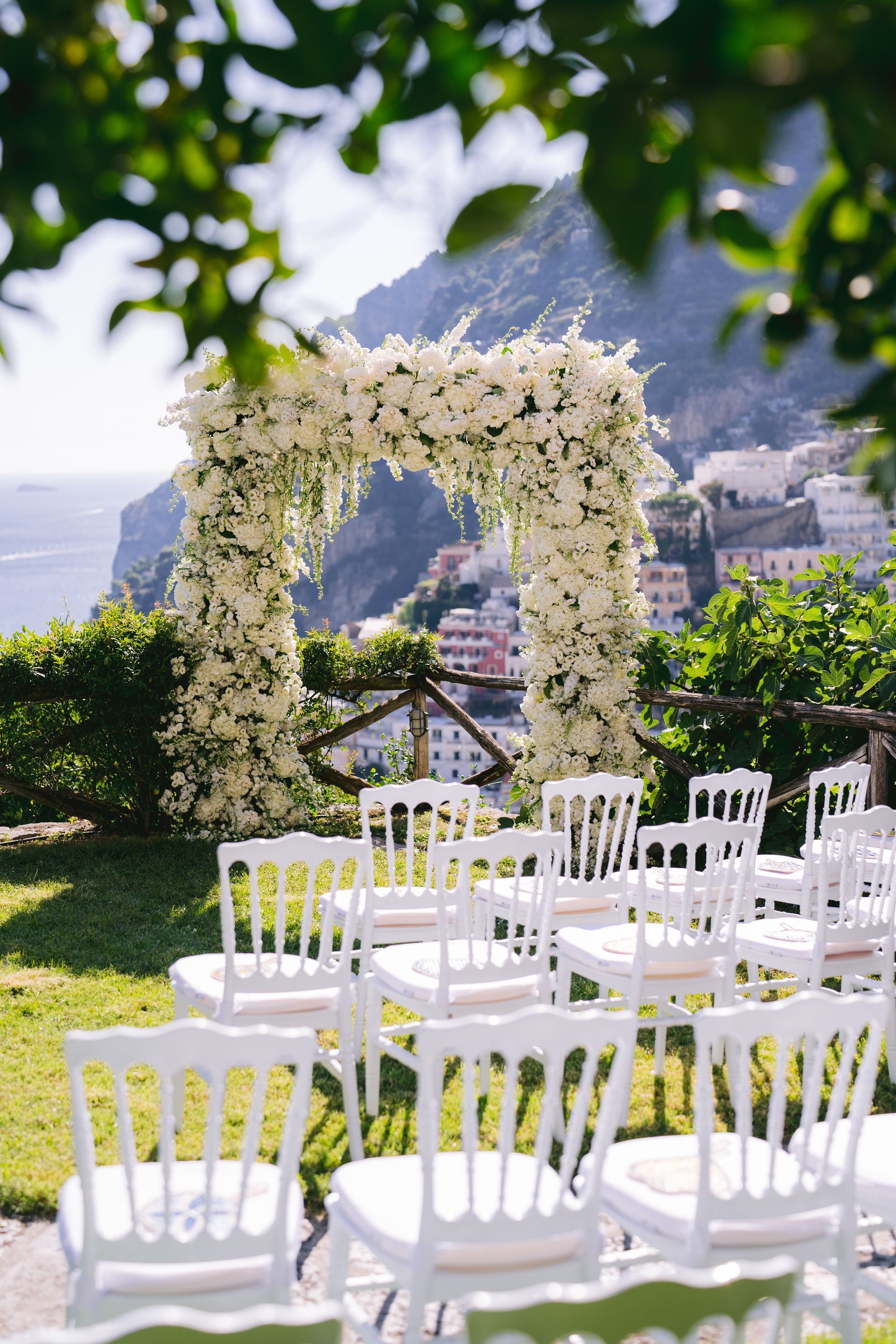 A row of white chairs are lined up in front of a floral arch.