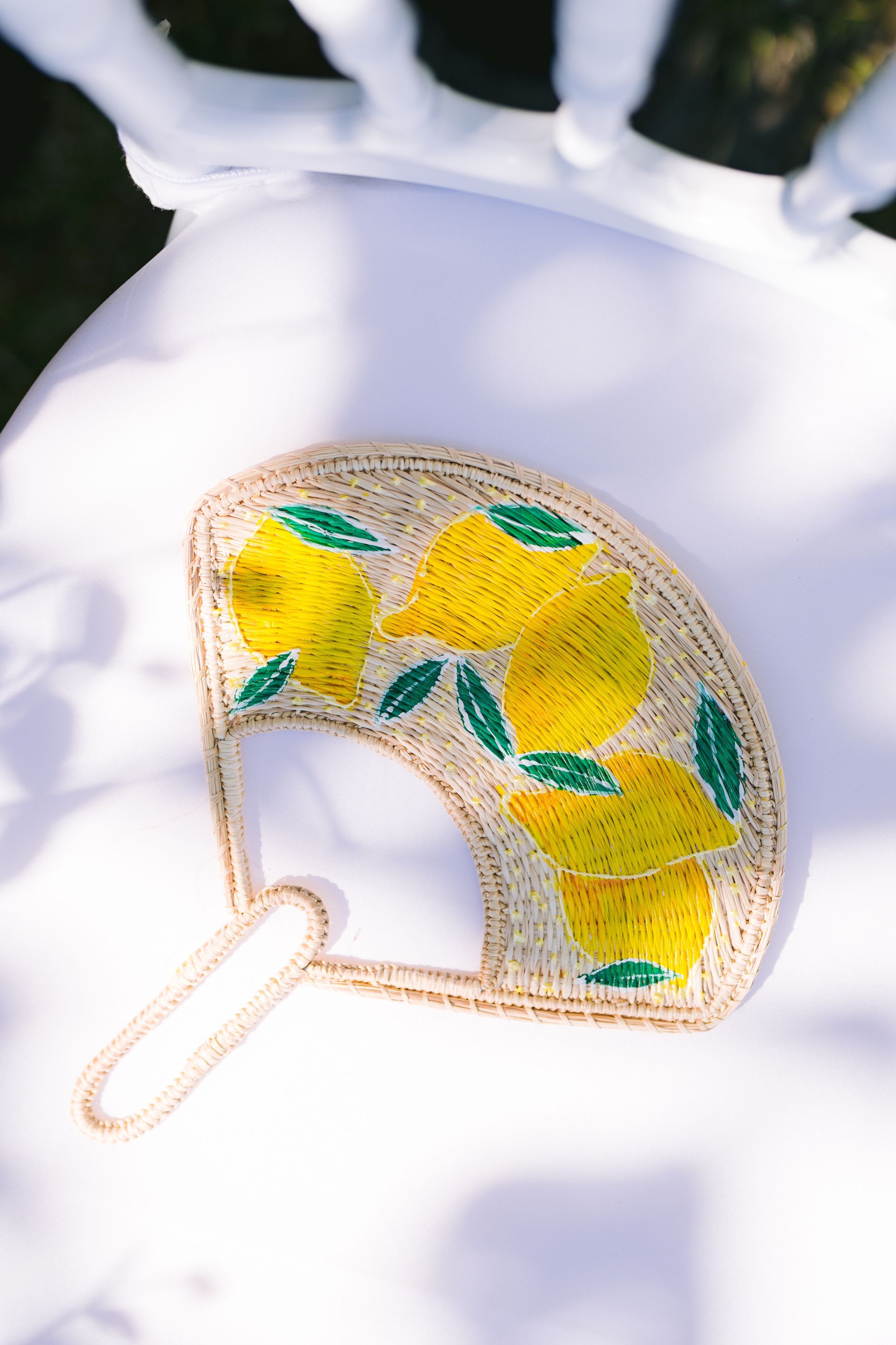 A fan with lemons on it is sitting on a white chair.