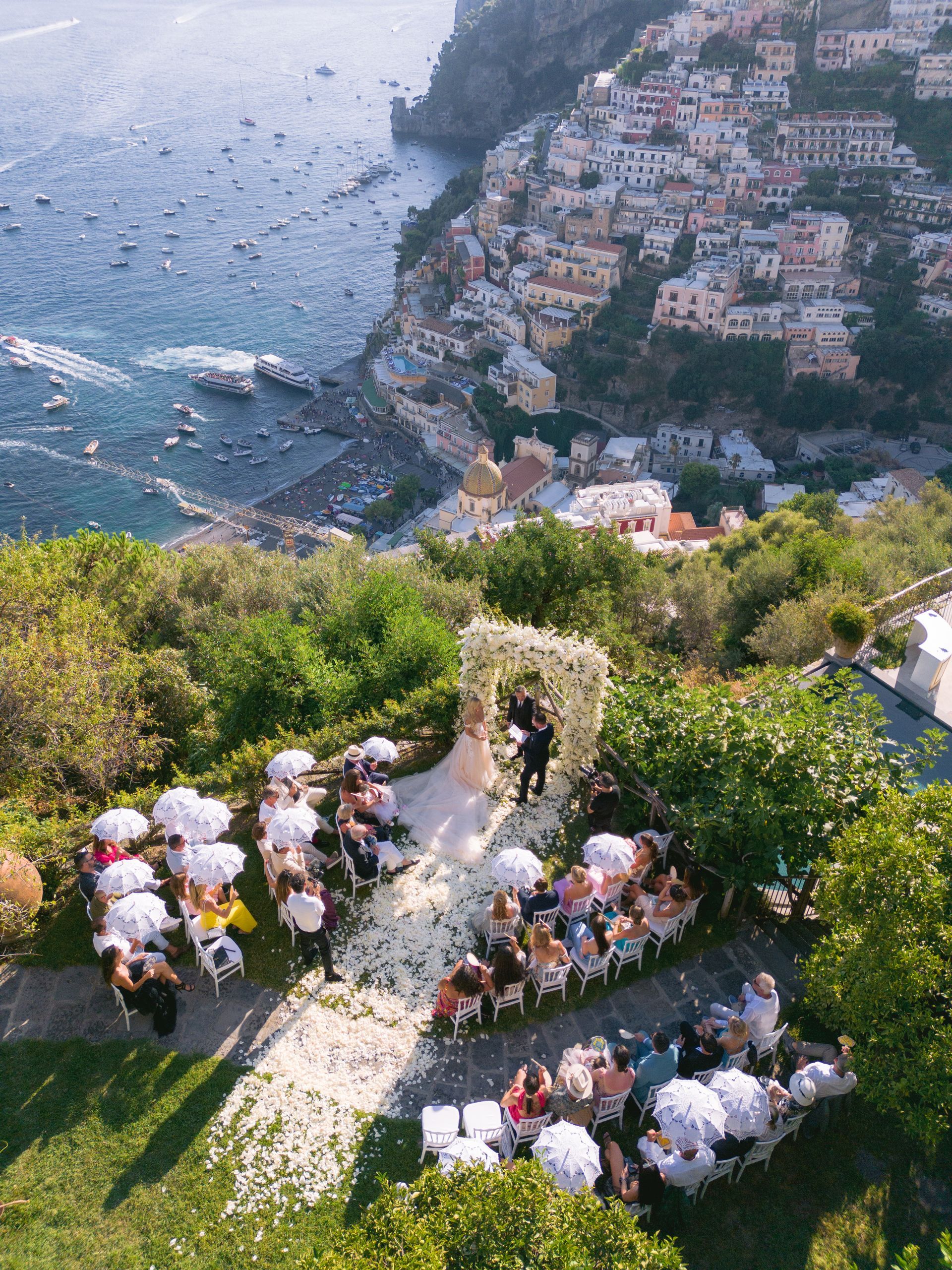 An aerial view of a wedding ceremony on top of a hill overlooking the ocean.