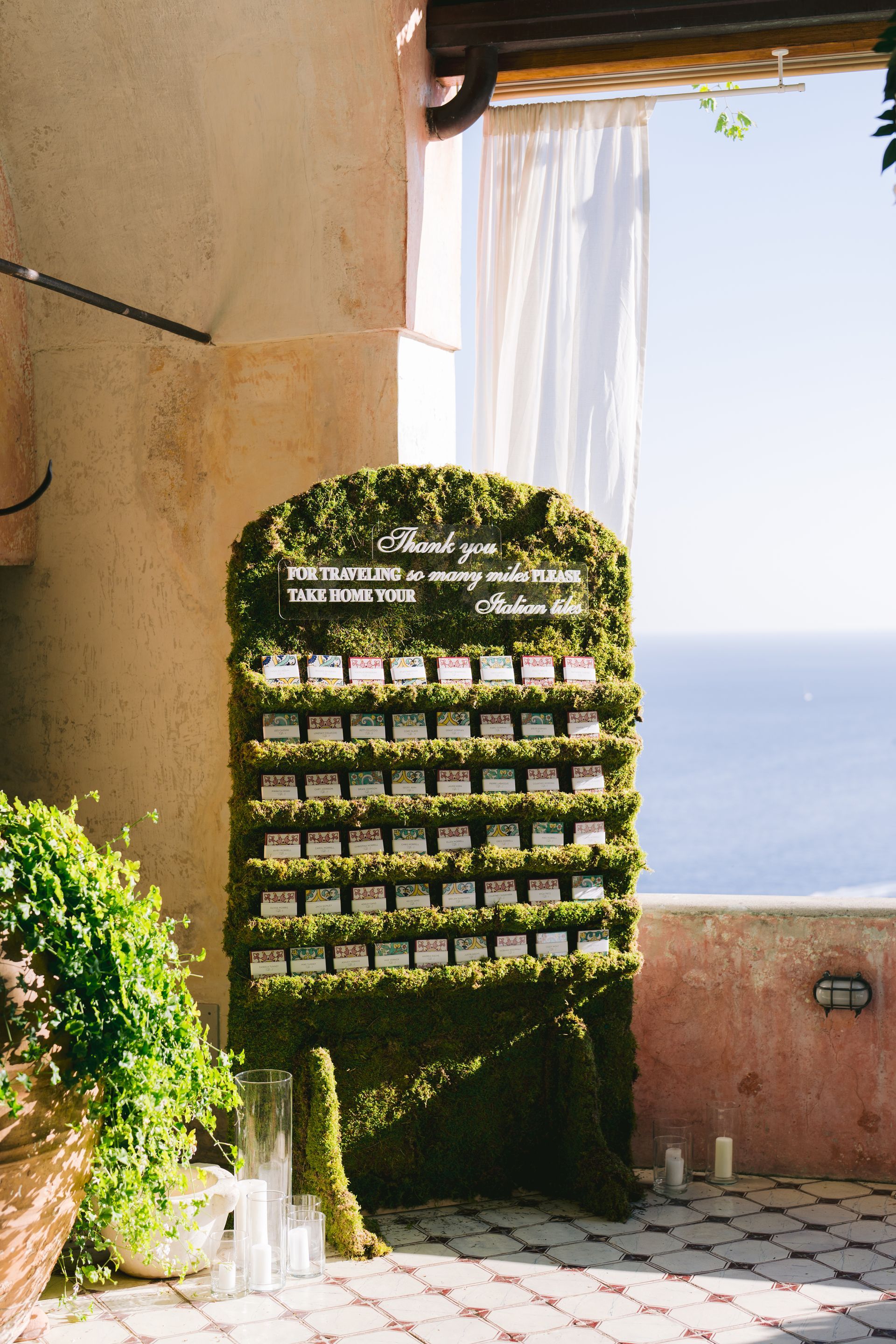 A seating chart made of moss is sitting in front of a window overlooking the ocean.