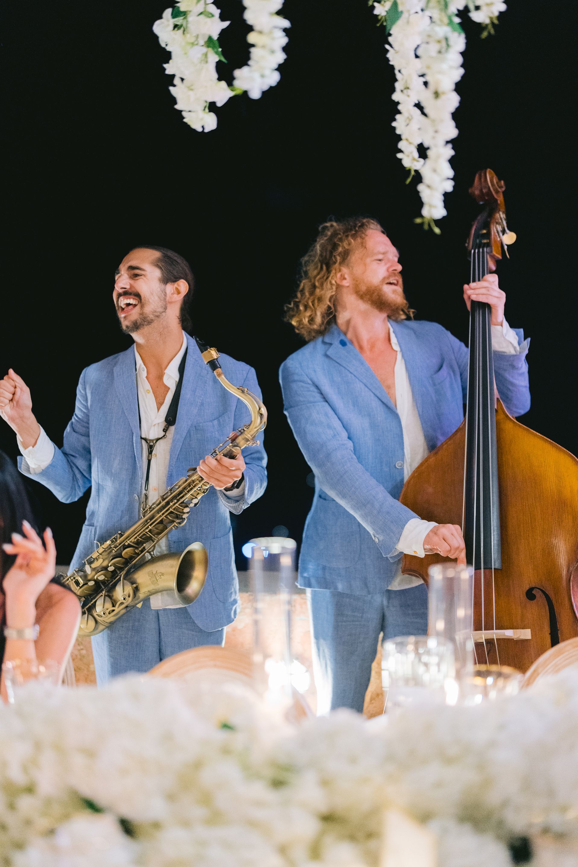 Two men are playing saxophones and a double bass at a wedding reception.