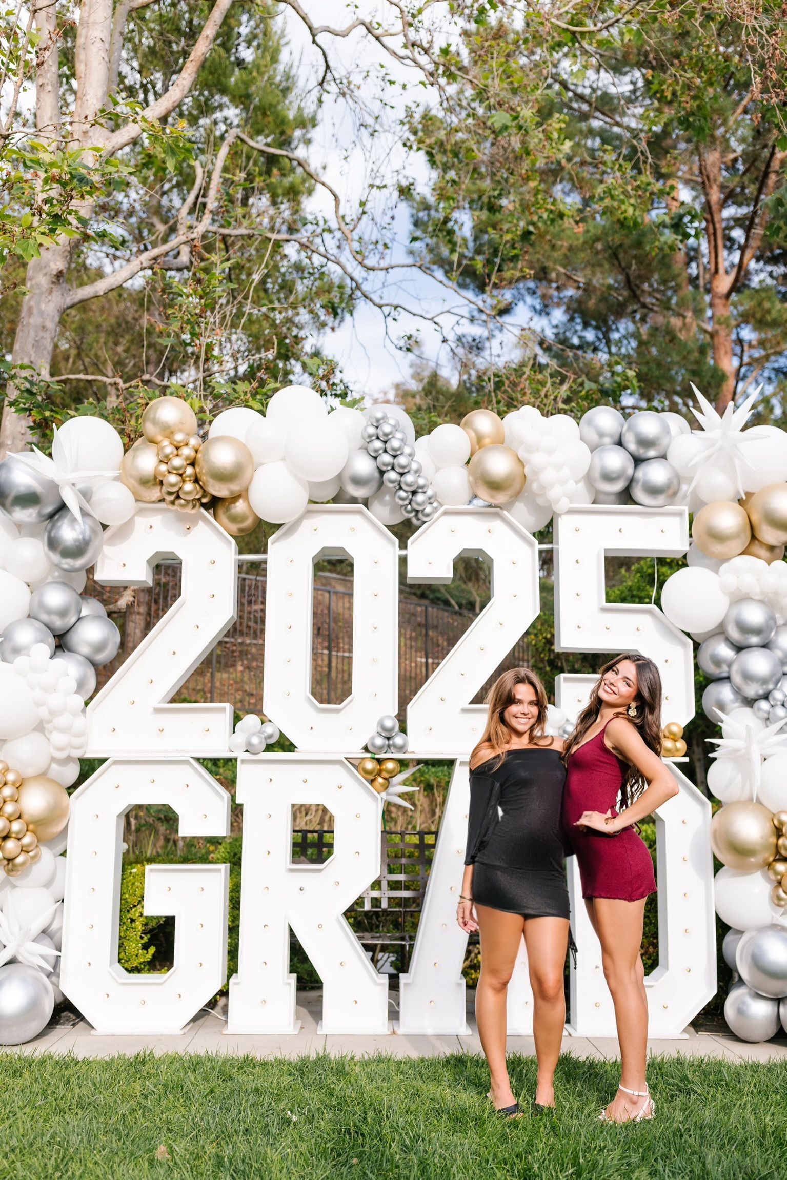 Two women are standing in front of a sign that says 2025 graduation.