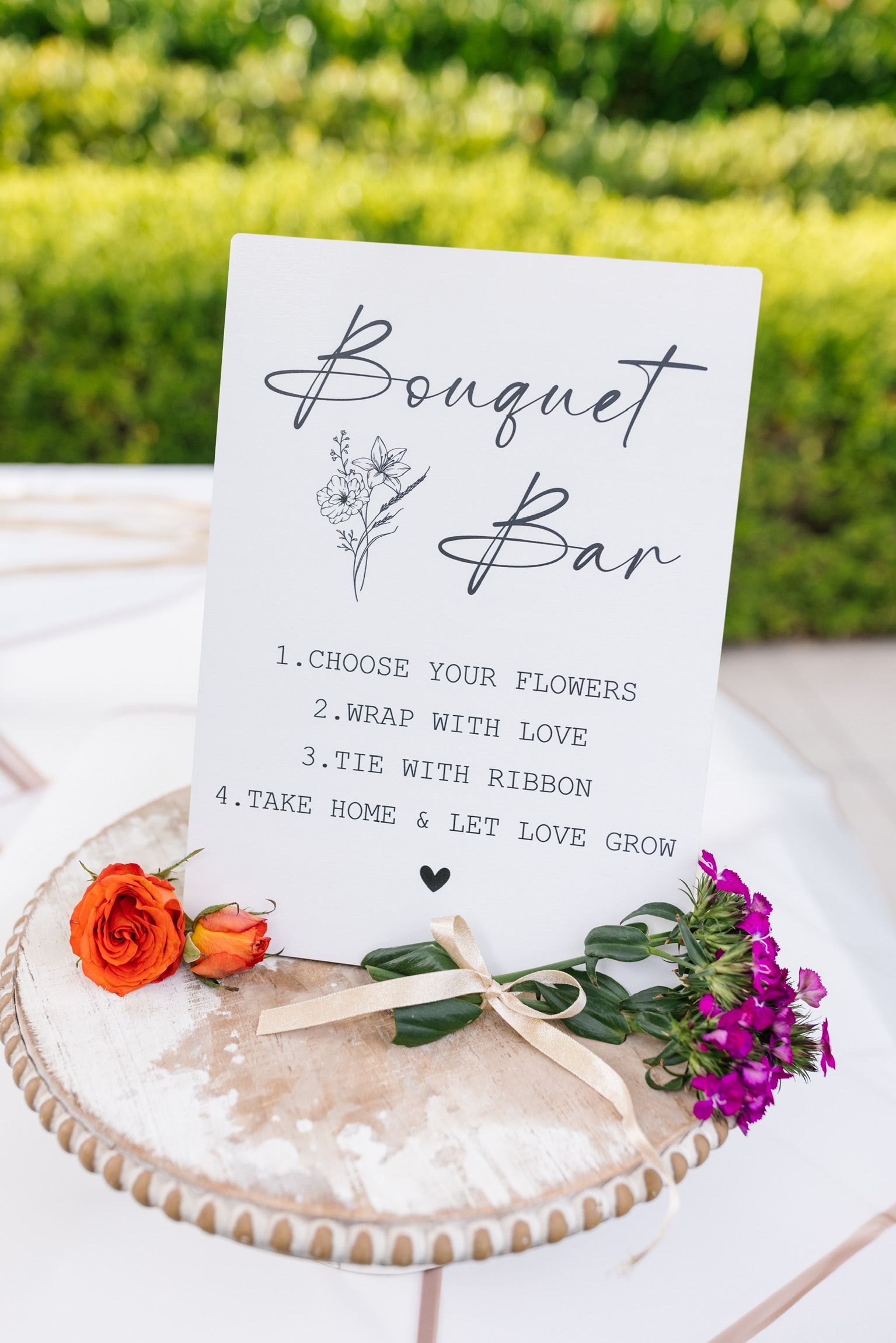 A sign that says bouquet bar is on a table with flowers.