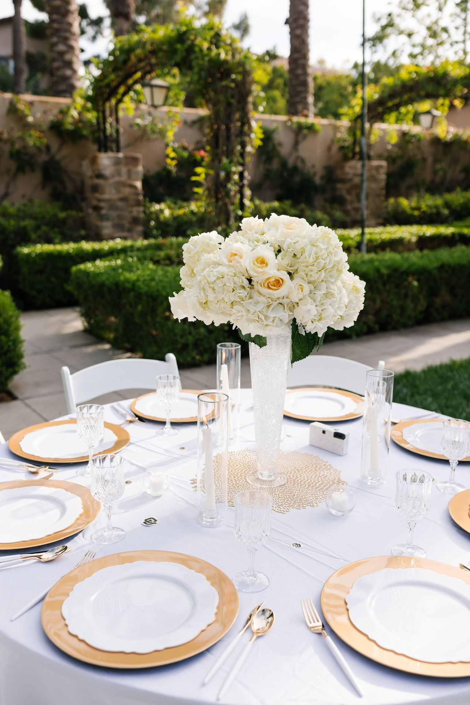 A table set for a wedding reception with white plates and gold chargers.